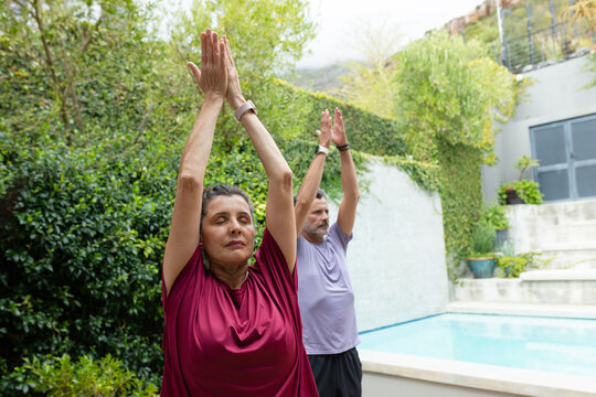 Senior couple stretching together practicing yoga beside residential pool with fitness watches