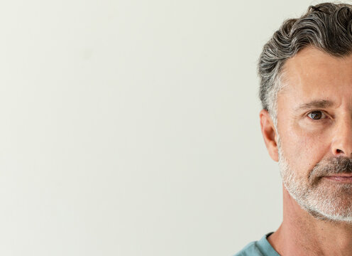 Mature man posing in teal crewneck shirt against plain wall, showing facial texture, copy space