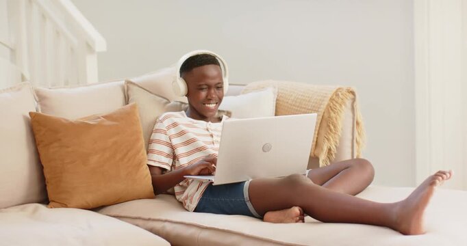 African youth male starting by smiling while typing on laptop, wearing white headphones on couch