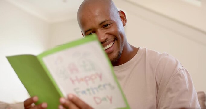 African American father-son sharing green border card for Fathers Day on couch, pointing at card