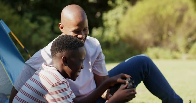 African American father and son sitting by blue tent son lifting binoculars while father teaching