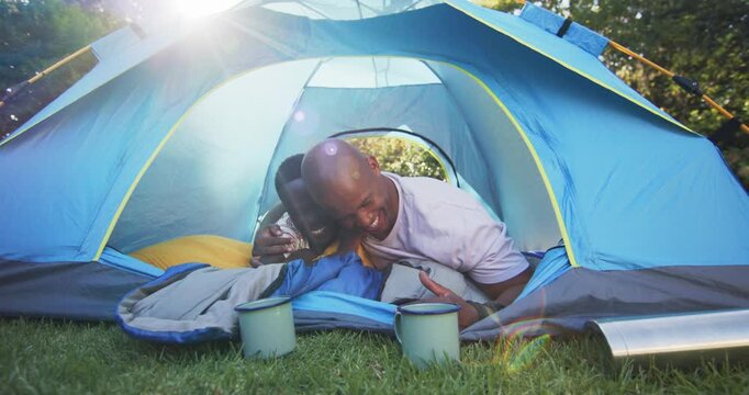 African American father and son waking, father rousing son, smiling to greet sun in blue tent