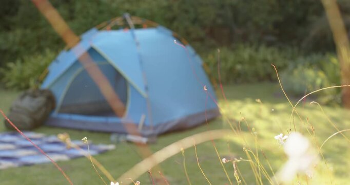 Camera pulling focus back revealing blue tent on lawn with blanket, pack, canisters showing gear