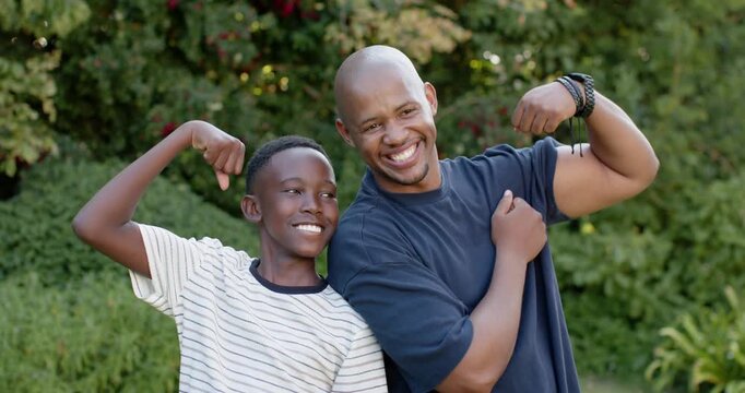 African American father and son after playful prompt, flexing arms, pointing at bracelets in garden