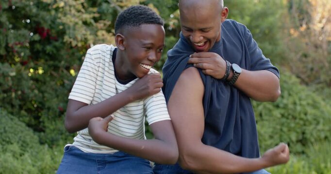 African American dad and son comparing arms on yard bench, son reaching, dad rolling navy sleeve