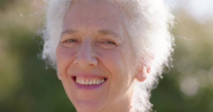 Senior woman looking at camera, smiling, laughing, squinting in garden sunlight, face with bokeh