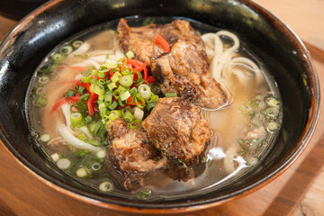 Traditional Okinawa Soba noodle soup with pork belly and ribs in a black bowl.