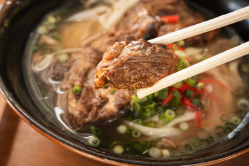 Traditional Okinawa Soba noodle soup with pork belly and ribs in a black bowl.