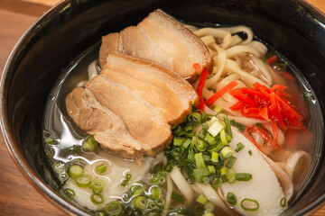 Traditional Okinawa Soba noodle soup with pork belly and ribs in a black bowl.
