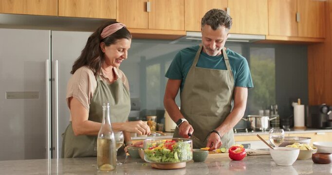 Diverse senior couple smiling, preparing salad for meal on island, feeding bite and checking flavor