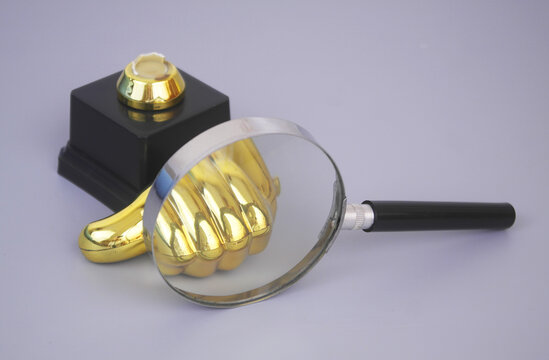 Broken golden thumbs up under magnifying glass on gey background. Dislike and change mind concept.
