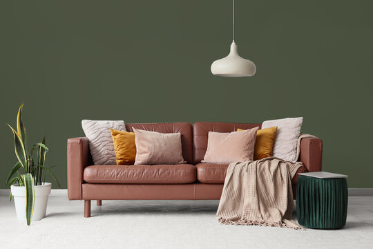 Interior of living room with brown leather sofa, houseplant and laptop on pouf