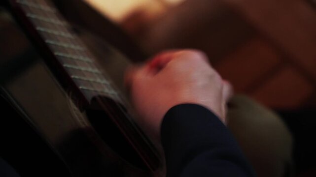 A person plays a guitar with care while sitting in a warm place. Their hands move skillfully over the strings