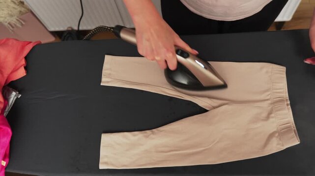 A person is using a handheld steam cleaner on a flat surface. The steam cleaner is being prepared for use on clothes