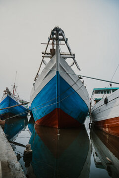 the imposing prow of a traditional Pinisi cargo ship at the historic Sunda Kelapa port in Jakarta. The composition emphasizes the scale and craftsmanship of the wooden vessel.