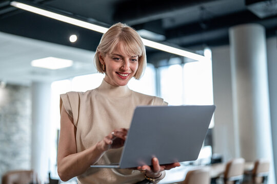 Smiling businesswoman using laptop standing in modern office