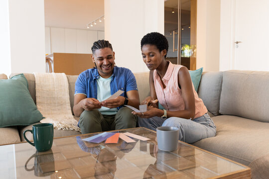 Diverse couple selecting paint swatches in living room, with two mugs on coffee table