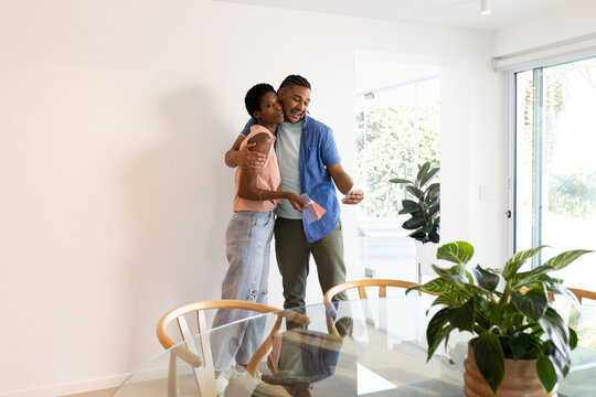 Holding paint color swatches, diverse couple standing in dining area by glass-top table