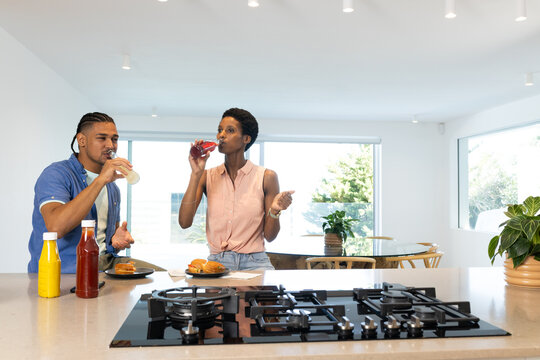 Standing African American couple holding burgers and drinks behind kitchen island, with gas cooktop