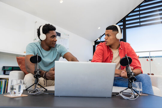 Recording diverse male friends leaning toward laptop in recording studio, with microphones