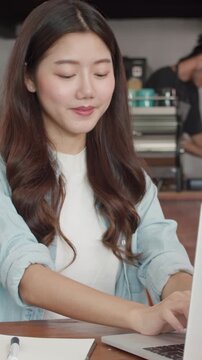 Vertical Screen : Young Asian freelance women working on laptop at coffee shop. Asian happy girl barista waiter wear gray apon serve hot cup of coffee to female customer who business work in cafe.