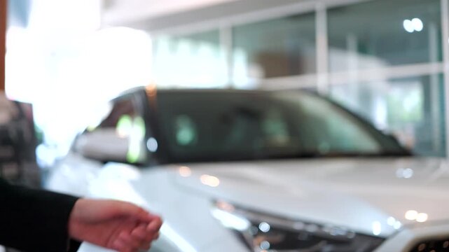 Close-up of car dealer handing over a key to a customer in a showroom. Successful vehicle purchase and ownership transfer. Automotive sales concept.