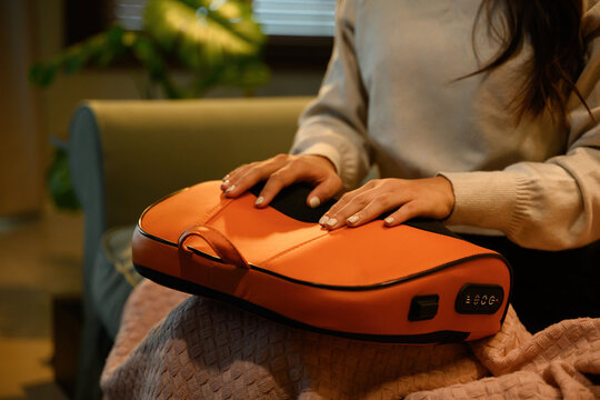 Close-up of an Asian woman placing her palms on a massage pillow, enjoying soothing relief and relaxation in a cozy home