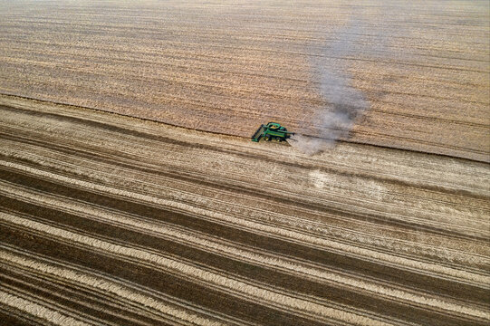 Aerial view of a combine harvester cutting a swathe through golden fields, plumes of dust rising in the summer heat, Chyhyryns'kyi district, Cherkasy Oblast, Ukraine.