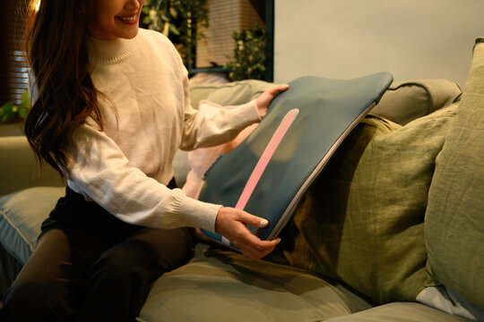 Close-up of an Asian woman placing a back cushion massager on a sofa, preparing for relaxation in a cozy living room