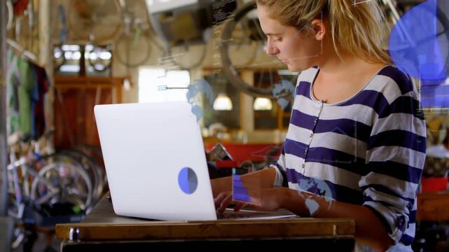 Woman typing laptop in workshop, initiating animated data maps, charts and analysis overlaying desk