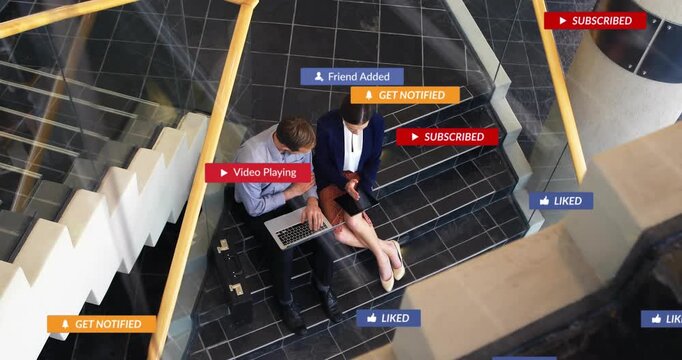 Two colleagues on steps reviewing laptop, tablet, tapping, causing social icons appearing, fading