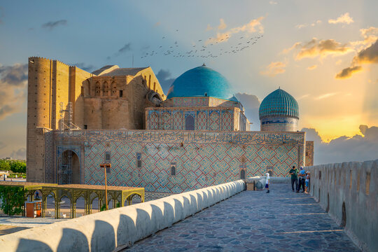 Turkistan, Kazakhstan - June 2, 2025: Golden hour view of the Mausoleum of Khoja Ahmed Yasawi (Hoca Ahmet Yesevi T&uuml;rbesi) from the historical wall with flying birds and sun rays