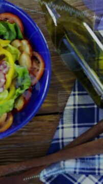 Vertical video: Camera pulling back from blue bowl, revealing salad, bottle, cloth for culinary