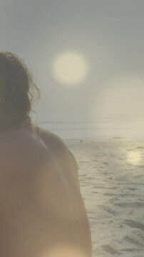 Vertical video: Low sun flare making cam panning in man moving showing wet back highlighting shore