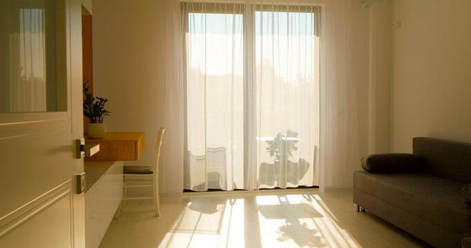Morning light streams through curtains in a cozy living room, casting soft shadows and creating a warm atmosphere. A peaceful start to the day.