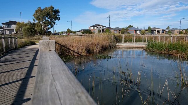 Wetland boardwalk in a suburban neighborhood in Lara, Victoria, Australia, with water, reeds, and modern houses in the background. Residential new estate with integrated green space, livable design.