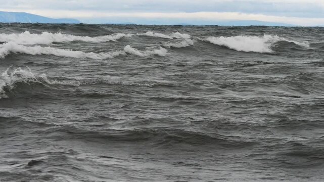  Big waves on the shore of lake Baikal against the background of distant mountains and overcast sky in a bad autumn day.
