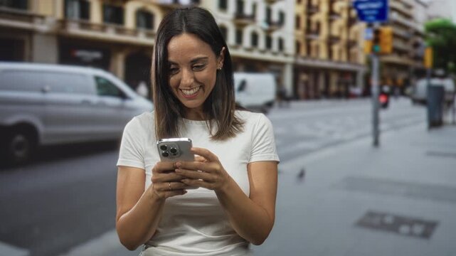 Woman holding smartphone and tapping screen, smiling with a small fist gesture on a city street in front of buildings and vans; joy connection.