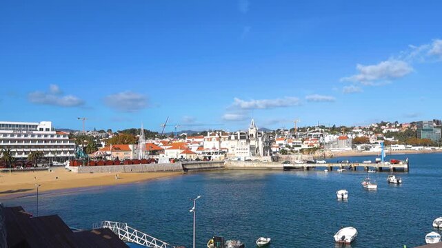 Stunning panoramic view of the bay of Cascais in Portugal, featuring the sandy Conceicao Beach, boats floating on the blue Atlantic Ocean, and the historic Seixas Palace on a sunny day