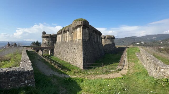 Wide view of Fortezza di Sarzanello in Sarzana, Liguria, Italy, featuring the massive stone fortress, moat, and surrounding countryside.