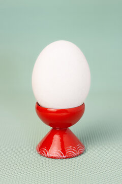 White chicken egg in red ceramic egg cup on blue green background vertical macro front view