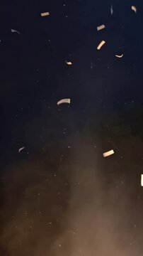 A slow-motion style video of rectangular golden and silver confetti pieces fluttering down through the air at night, illuminated by a light source from below