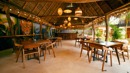 Tropical restaurant with woven lamps and string lights decorating the thatched roof. Painted jaguar mural on back wall © DMegias