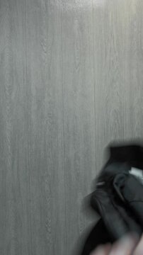 Black leather biker jacket displayed on light grey wooden plank floor from overhead perspective. Garment features multiple zippers, silver buttons, and classic collar design. Jacket lies unfolded, rea