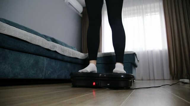 Low angle view of woman legs in black leggings white socks standing on black vibration platform for full body workout muscle toning home living room