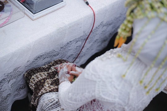 Traditional Indonesian bride's hands adorned with white henna during ceremony.