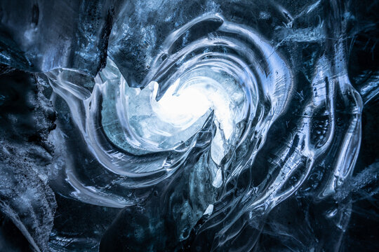 View of the icy cave's depth with spiraling ice formations, illuminated by ethereal light, beckoning exploration, Sveitarfelagio Hornafjordur, Iceland.