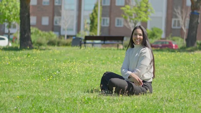 latin woman throwing a ball to her border collie dog while sitting on the grass