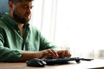 Man typing on keyboard while sitting at desk by window in a well-lit room © fotofabrika