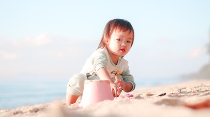 Fototapeta premium Beach play promoting early childhood development, sensory exploration, and creative learning. Asian toddler girl playing with sand toys by the sea, enjoying outdoor activity and natural discovery.
